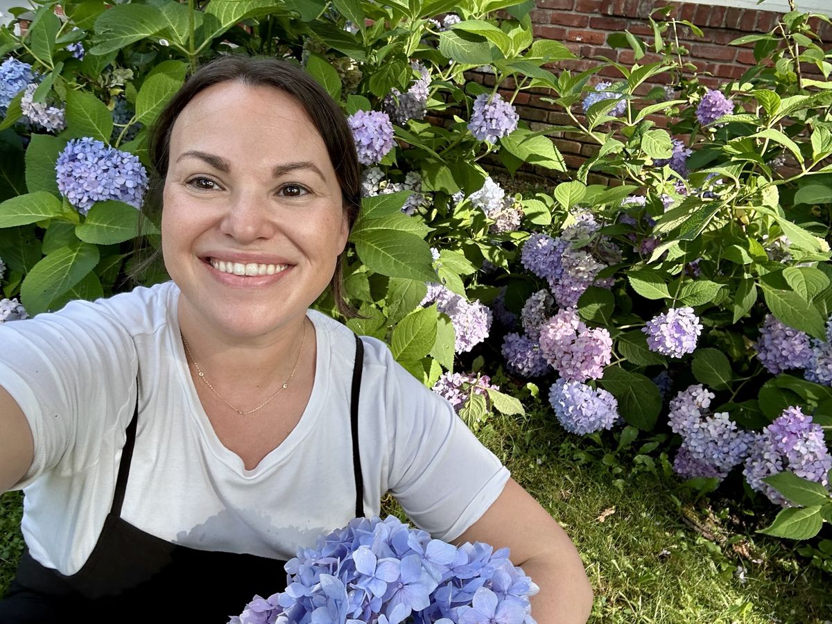 Danielle Shoolbraid smiling among blue and lilac hydrangeas in her garden